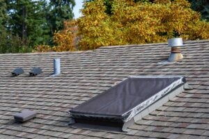 A professional inspects a residential shingle roof with a clipboard and visible roofing materials nearby.
