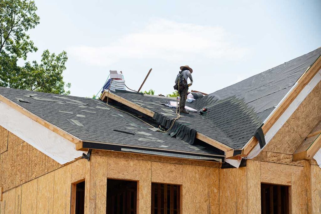 Roofing worker rolls protective underlayment across a wood roof deck before shingles are installed.