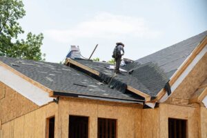 Roofing worker rolls protective underlayment across a wood roof deck before shingles are installed.